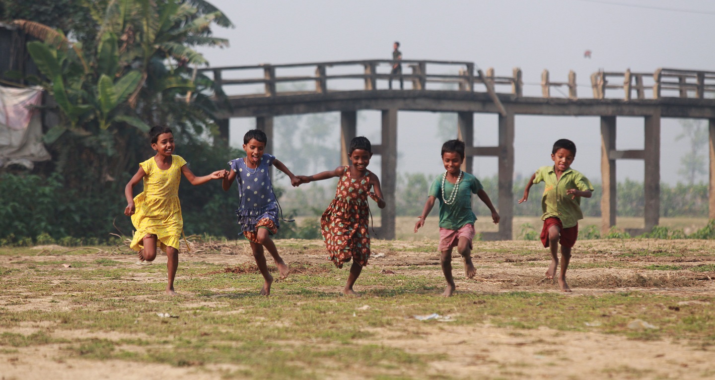 Kids holding hands and running in a field.