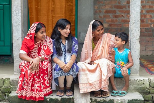 Three women and a young boy smile in front of their home in Bangladesh