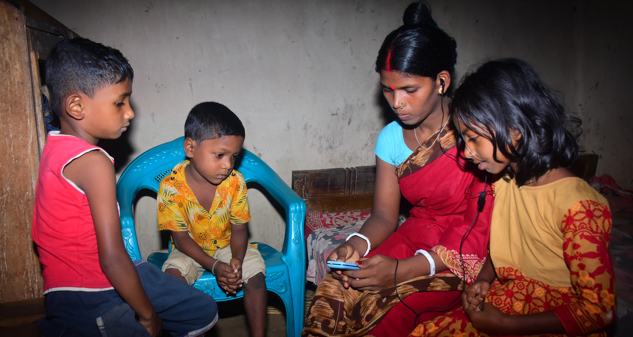 A woman in Bangladesh listens to educational audio on a phone with three children