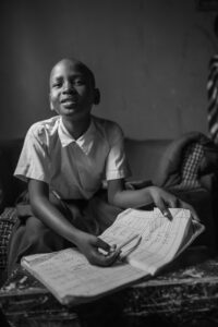 Amina, a former Play Lab participant, looks up from writing in a homework book from her elementary school