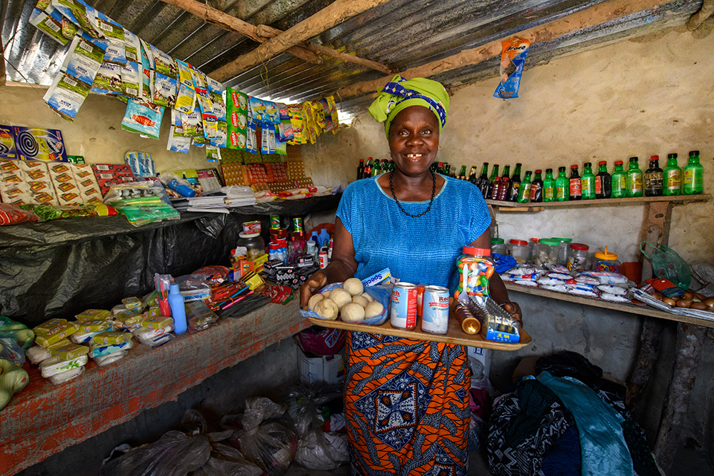 Kumba, a participant of BRAC's Graduation program in Liberia, smiles in her shop while she holds up a tray of her products