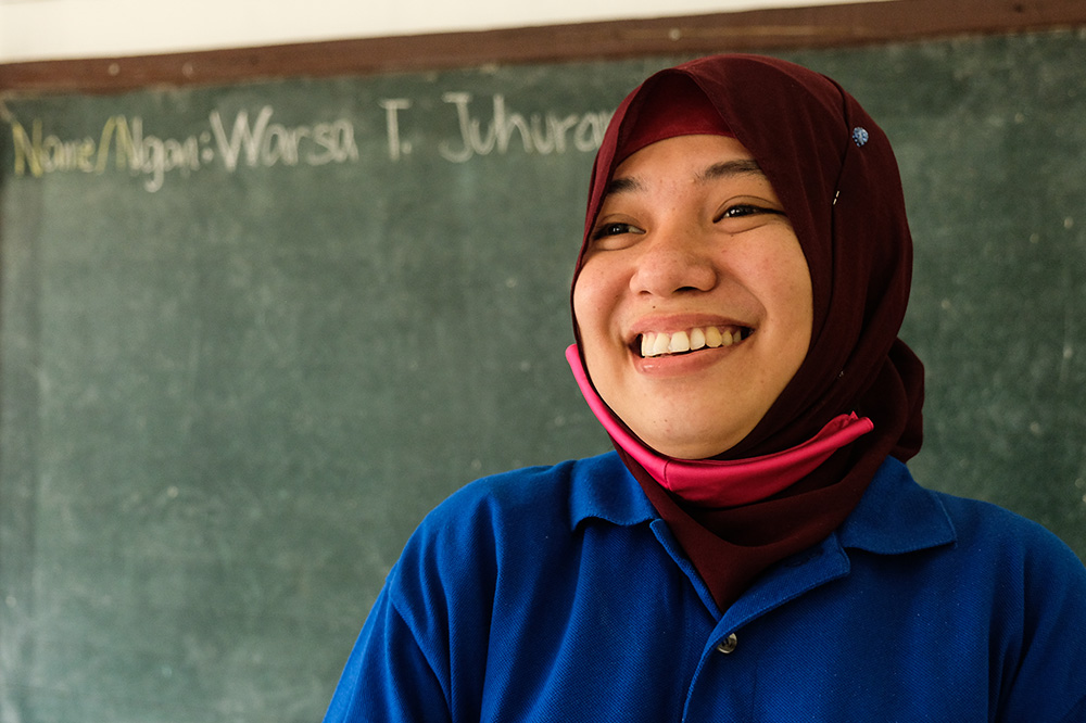 A BRAC teacher in the Philippines smiles in front of a chalk board