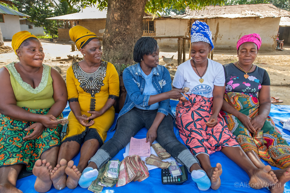 Jebbeh hands money to a credit officer during a microfinance group meeting as three other borrowers look on. Photo by Alison Wright.