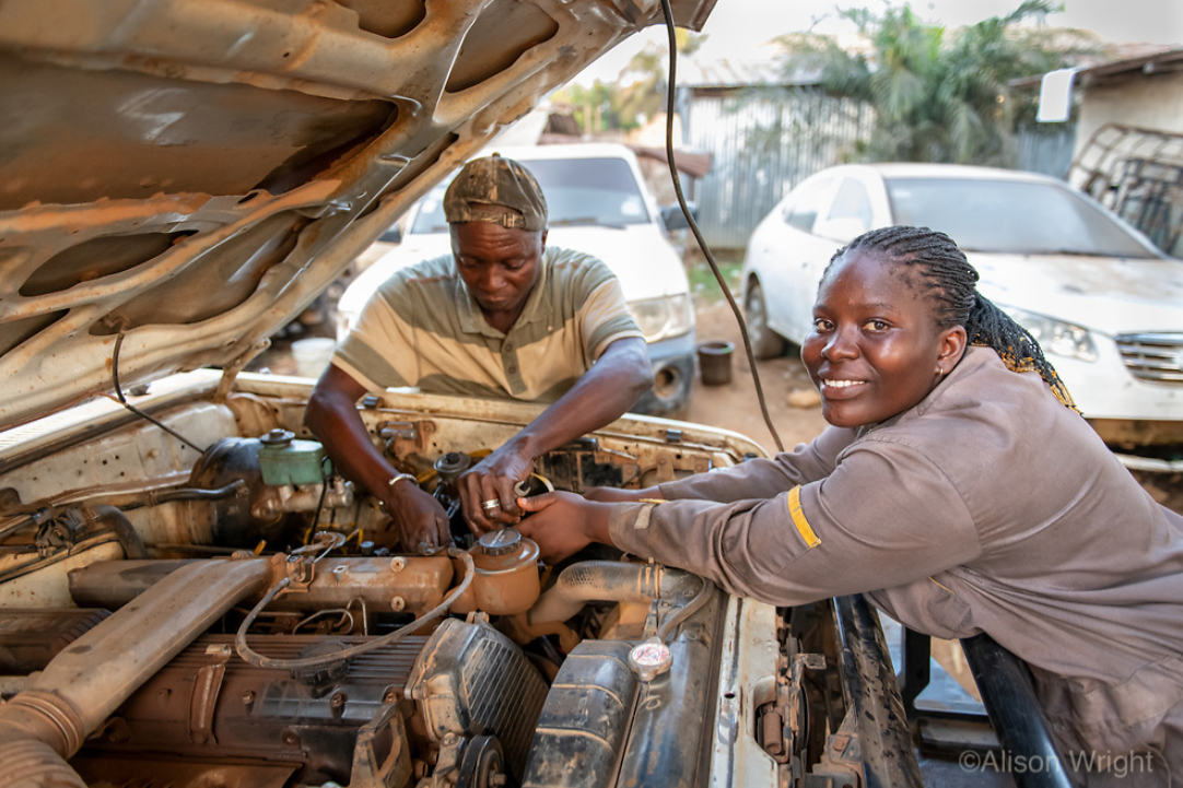 Josephine works on the hood of an open car while one of her mentors works alongside her. Photo by Alison Wright.
