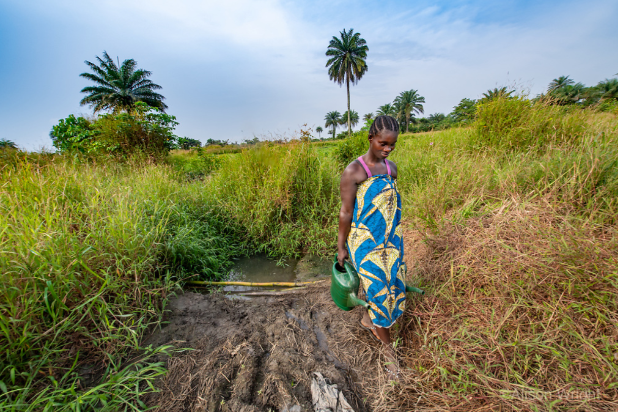 Patience carries watering cans to water her crops