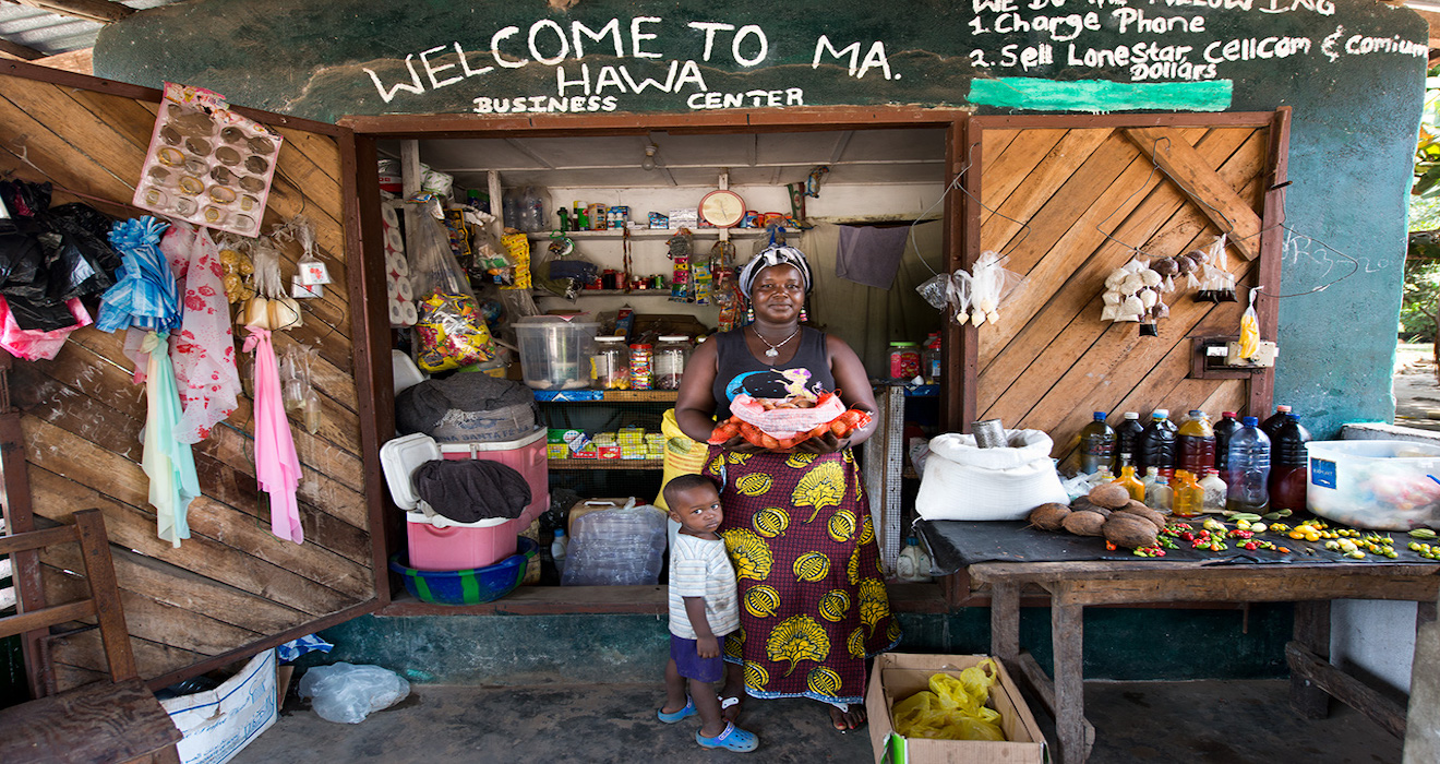 Woman and small child standing in front of a small grocery shop.