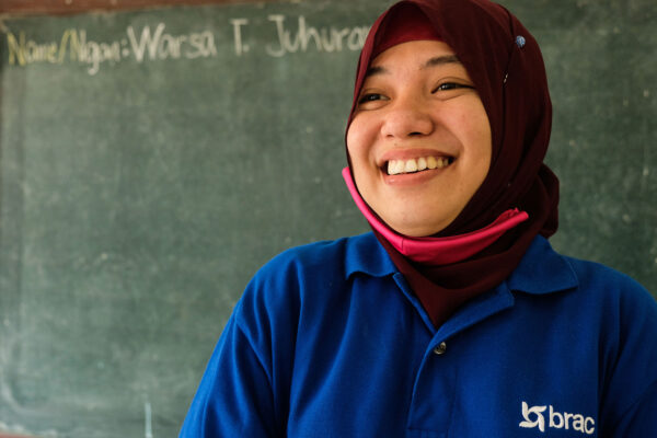 Close up portrait of Warsa, a teacher in a BRAC learning center in the Philippines, smiling in front of a chalkboard