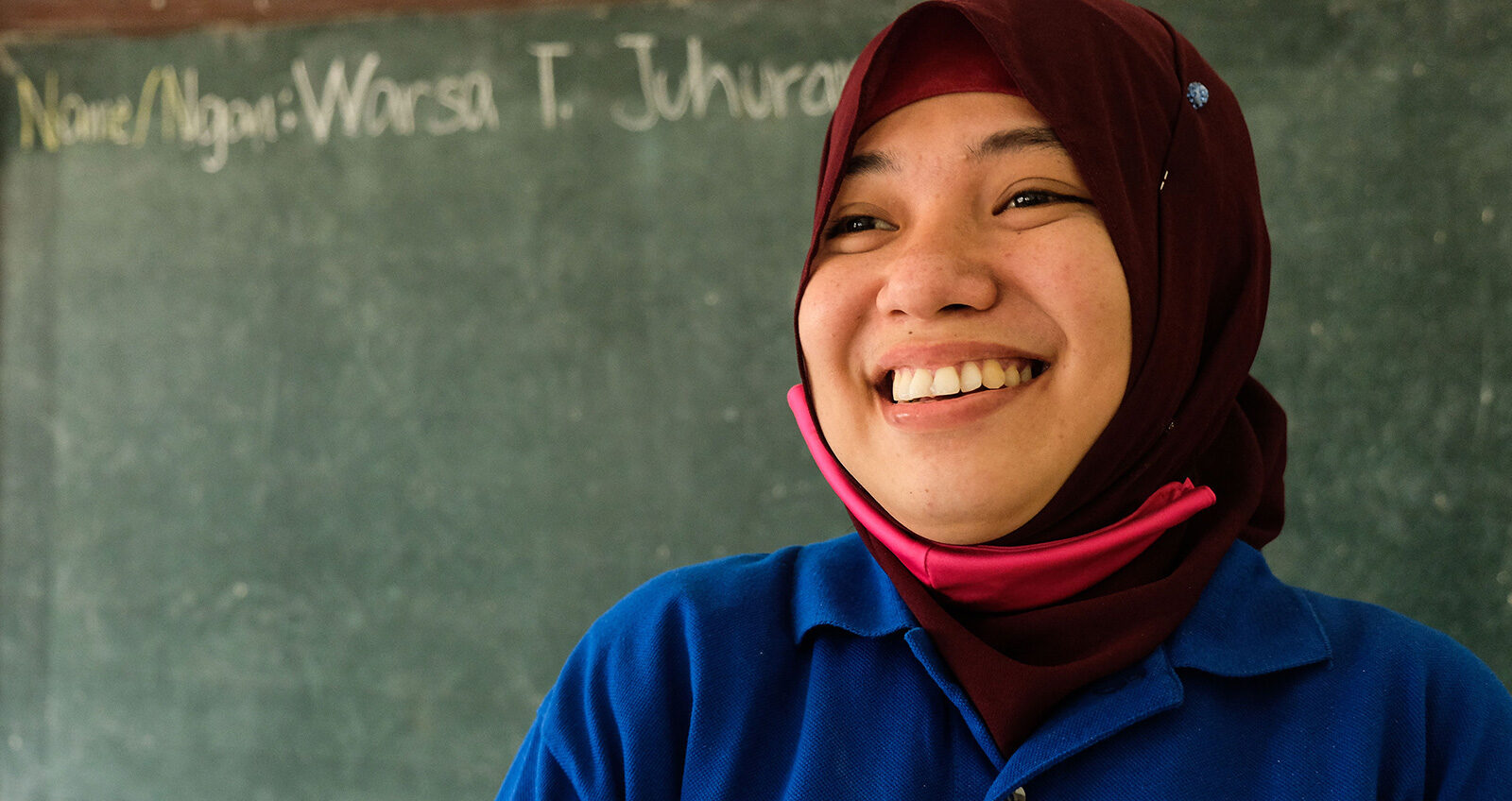 Close up portrait of Warsa, a teacher in a BRAC learning center in the Philippines, smiling in front of a chalkboard