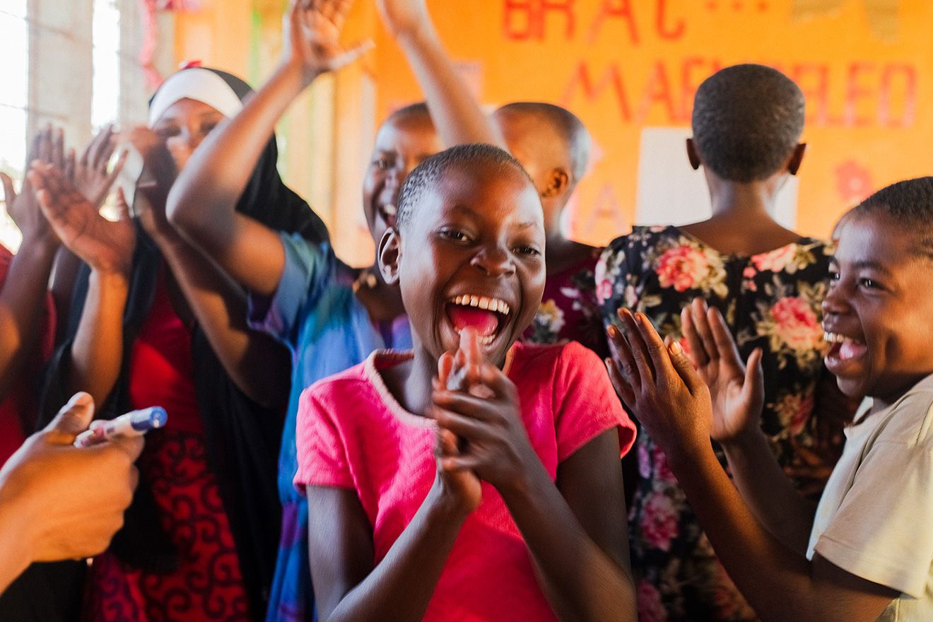 A girl in an AIM youth empowerment club in Tanzania smiles and claps