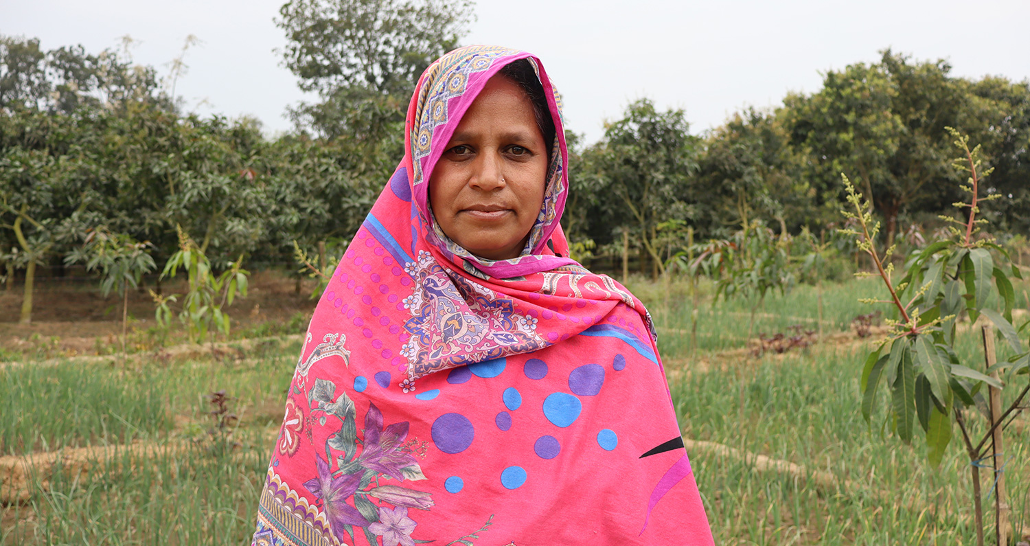 Marjina, a farmer in Bangladesh, poses in front of her land.