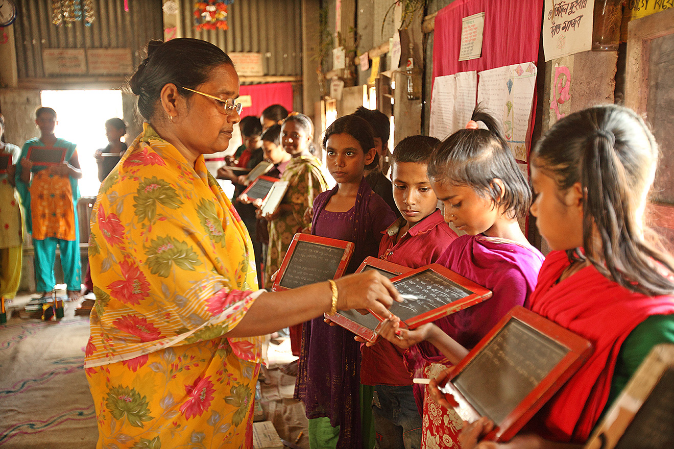 A teacher in a BRAC school works with a small group of four students who each hold small chalkboards