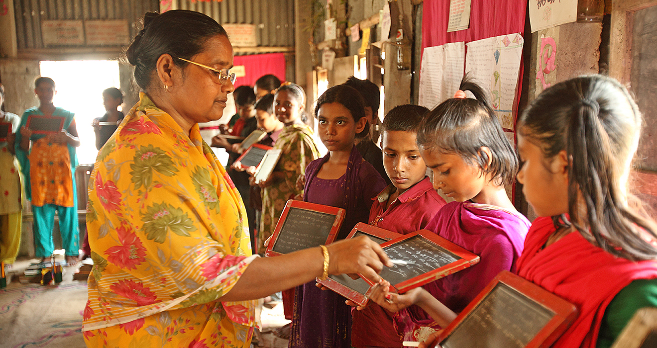 A teacher in a BRAC school works with a small group of four students who each hold small chalkboards