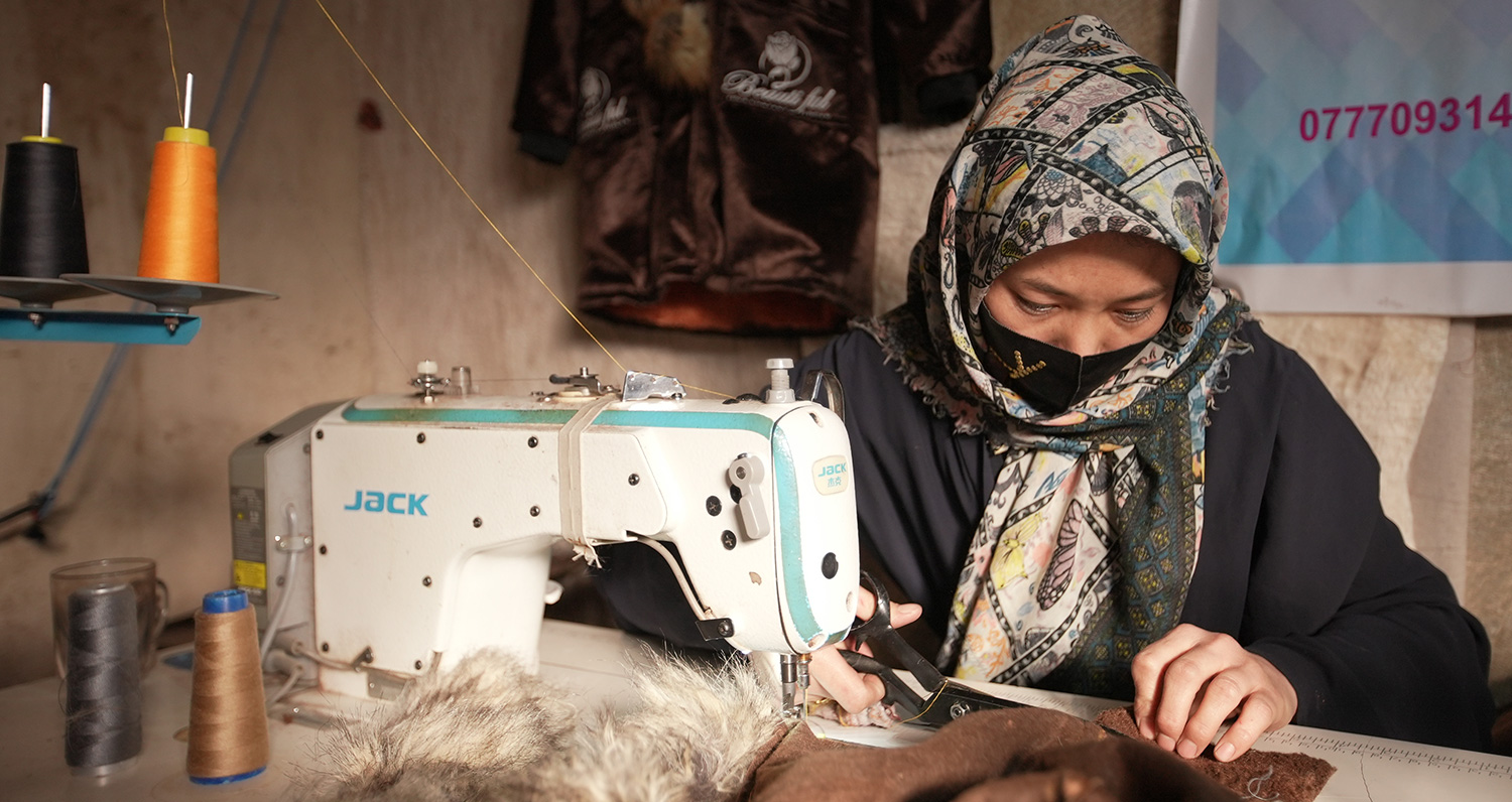 Zainab, a tailor in Afghanistan, sews a coat at her sewing machine.