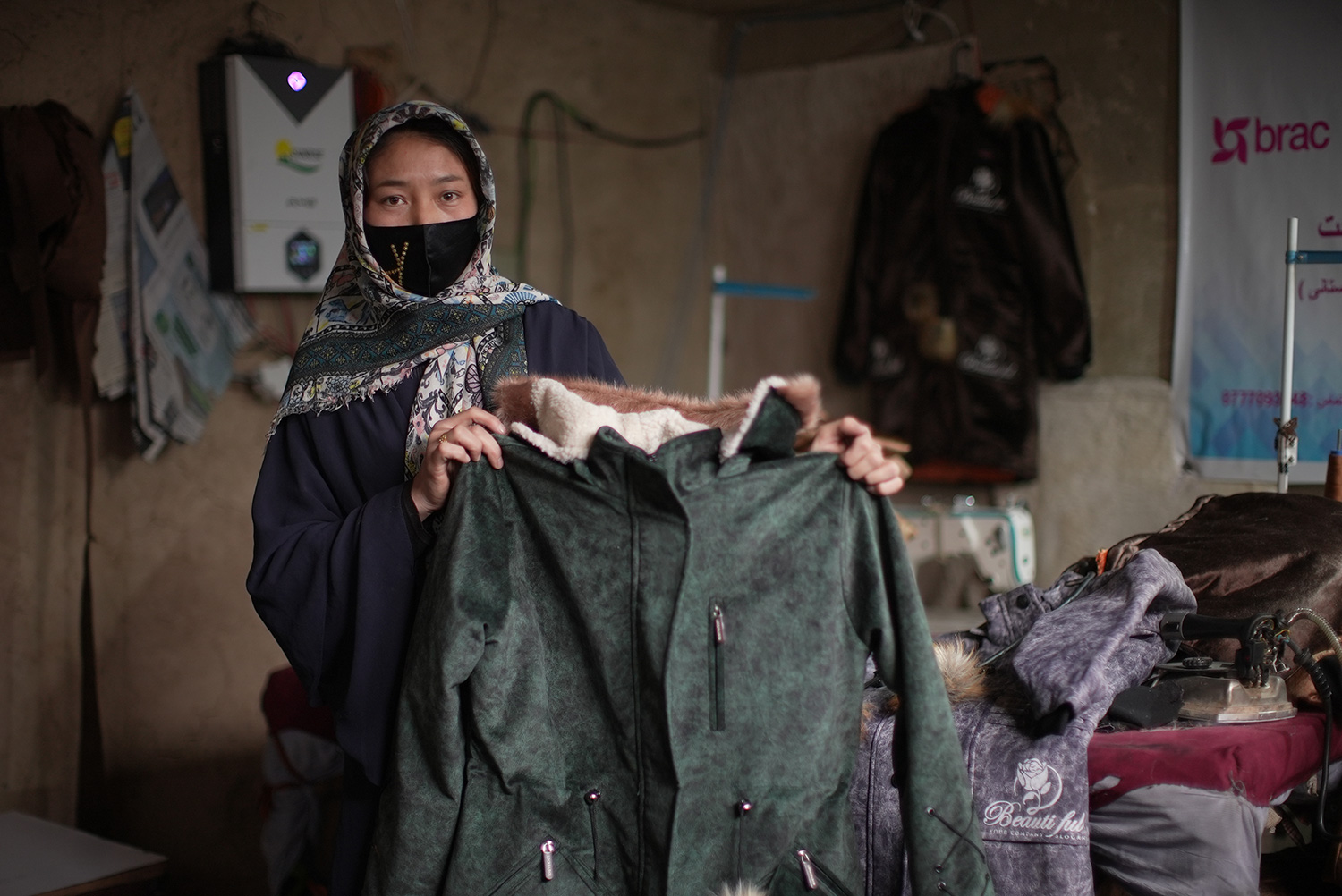 Zainab, a tailor in Afghanistan, proudly holds up a finished coat she made.