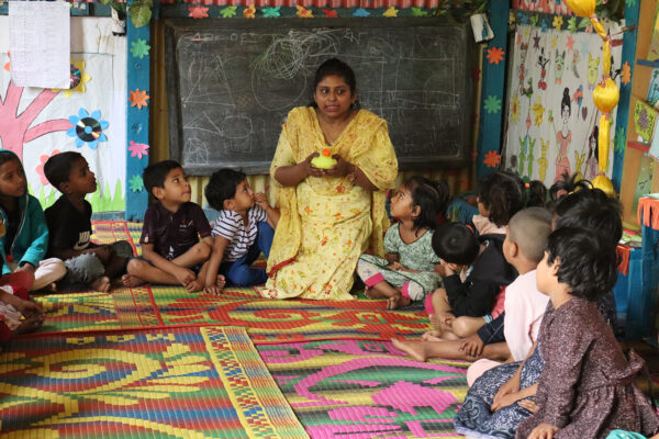 Amena, a Play Leader in a Play Lab in Dhaka, describes an activity holding a rubber duck while children sit in a circle and listen.