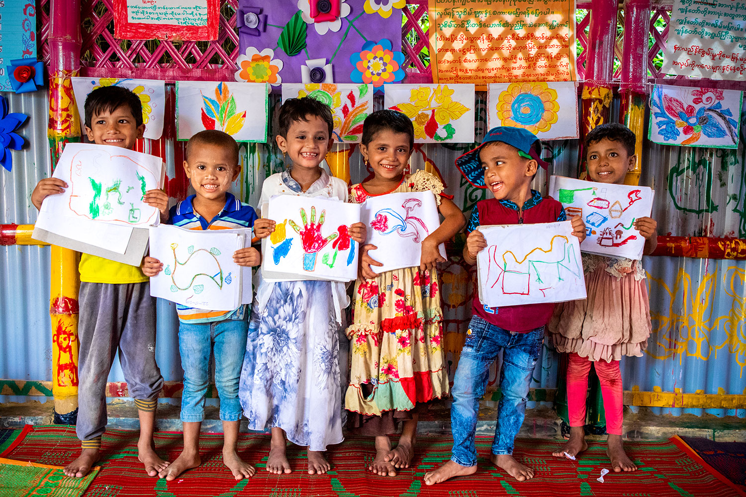 Rohingya refugee children smile with their artwork at a Humanitarian Play Lab in Cox's Bazar, Bangladesh
