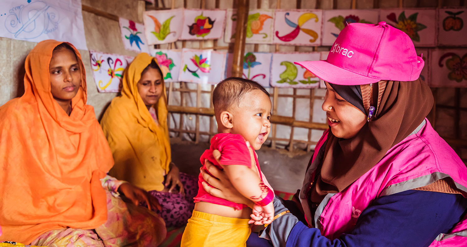 A community health worker in the Rohingya refugee camp holds a happy refugee baby
