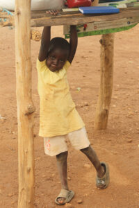 Annet's daughter, Emma, hangs off of the wood poles of Annet's shopn stall