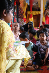 A Play Leader in a Play Lab in Dhaka reads to a group of onlooking children.