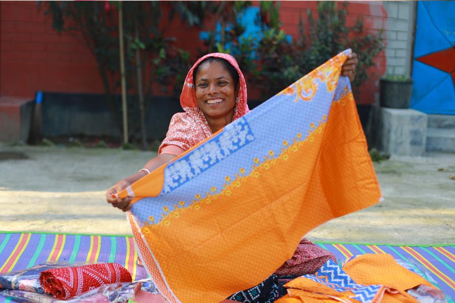 A returnee migrant shows off her small business, proudly holding up a piece of fabric she's sewing.