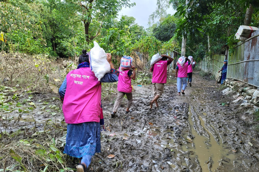 Four BRAC staff march through muddy flooded grounds holding food aid sacks to deliver.