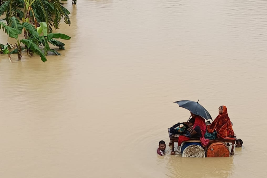 August 25, 2024: Two men guide a makeshift raft carrying two women and a child through neck-deep water in Fulgazi, Feni. This is just one of the 1.2 million families left stranded by Bangladesh’s worst flood in three decades.