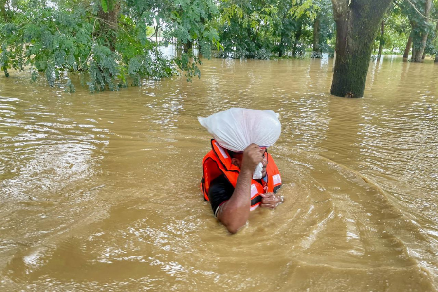 August 24, 2024: A BRAC frontline staff member wears a life jacket as he wades through chest-deep water to deliver aid supplies to families affected by the floods. BRAC teams are delivering critical food, baby food, drinking water, health and hygiene products, and livestock feed to families in need of urgent support. 