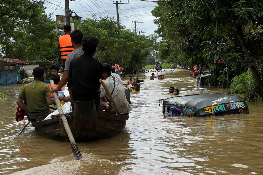 August 23, 2024: A team carrying aid packages travels by boat down a flooded street, passing a nearly submerged tuk-tuk and passersby wading through chest-deep water. As flooding ruins roadways like this one, many communities are entirely cut off from aid, which is why it’s critical for BRAC teams to use all forms of transportation to reach families.