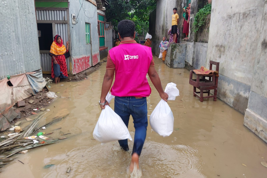 August 25, 2024: A BRAC staff member walks through an alley flooded with shin-deep water to deliver food kits to local families in Muradnagar Upazila, Comilla. Many families have remained in homes with knee-deep water.