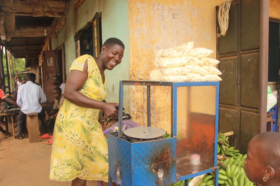 Juliet, a young woman in BRAC's youth empowerment program in Uganda, stands behind her popcorn machine to prepare a bag of popcorn for a young customer.