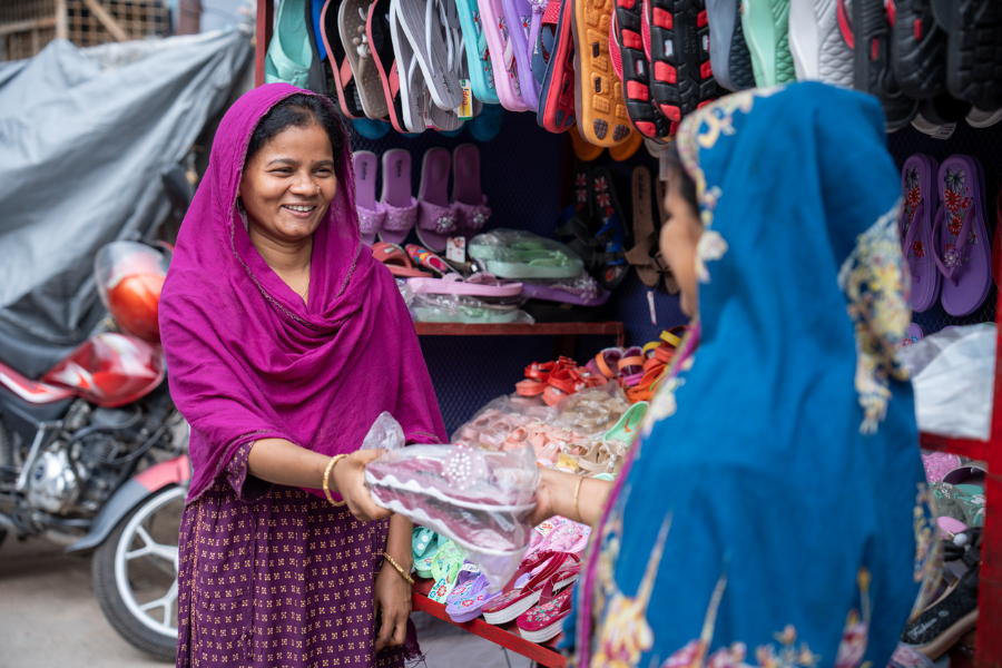 A participant in BRAC's Ultra-Poor Graduation program hands a pair of shoes she's sold to a customer outside her shoe store.