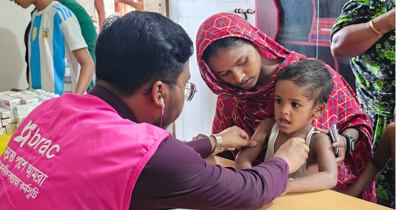 A BRAC medical personnel treats a child who sits on his mother's lap.