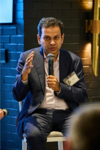 Asif Saleh, Executive Director of BRAC, speaks into a microphone while sitting on a stool at an UN week side event.