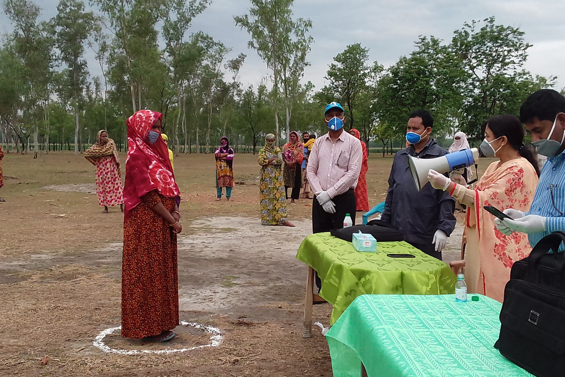 A participant of BRAC's Ultra-Poor Graduation program stands in a circle outlined on the ground wearing a mask as she works with masked BRAC staff six feet away.