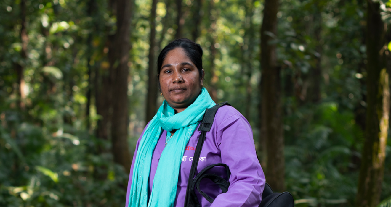 Nilafur Yasmin poses on a forest path in her community health worker uniform.