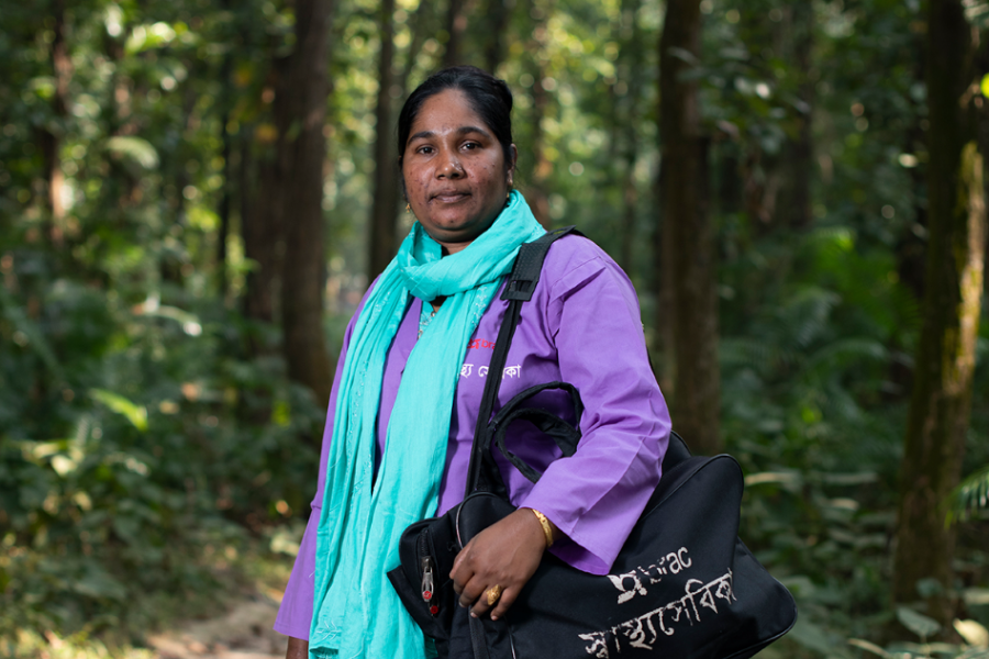 Nilafur Yasmin poses on a forest path in her community health worker uniform.