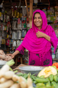 Shahinur hands potatoes to a customer out of frame at her produce shop.