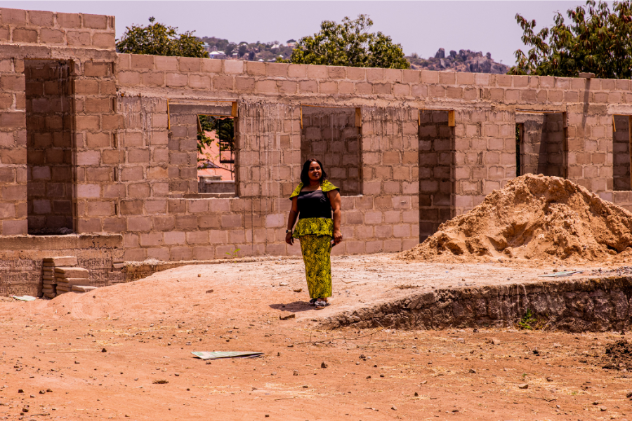 Queenfrida stands in front of a cement block building under construction, the site of her future school expansion.