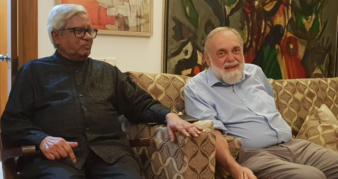 Dr. Richard cash, right, sits on a chair next to BRAC Founder Sir Fazle Hasan Abed, left, as they both smile.