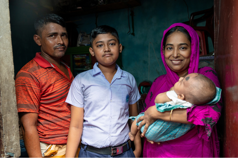 Left to right: Shahinur's husband, her eldest son, Shahinur, and her baby (held in Shahinur's arms) pose and smile in their home.