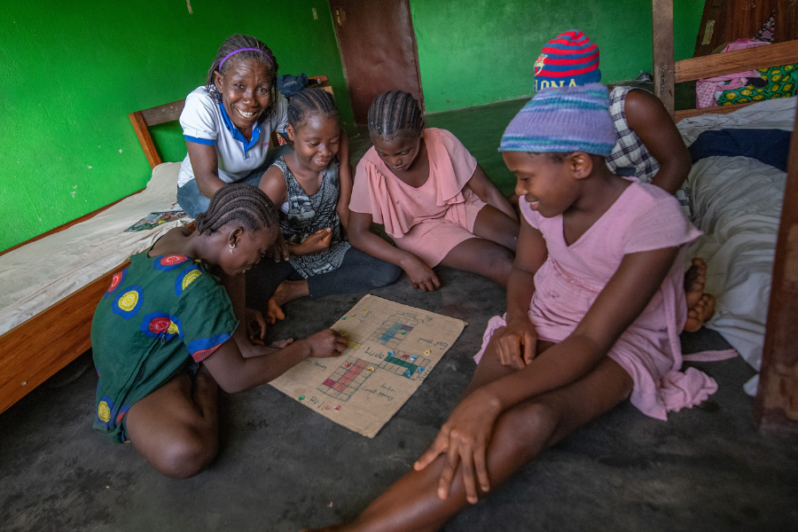 Selena sits with a group of five girls from the home as they play a board game in their bunk room.