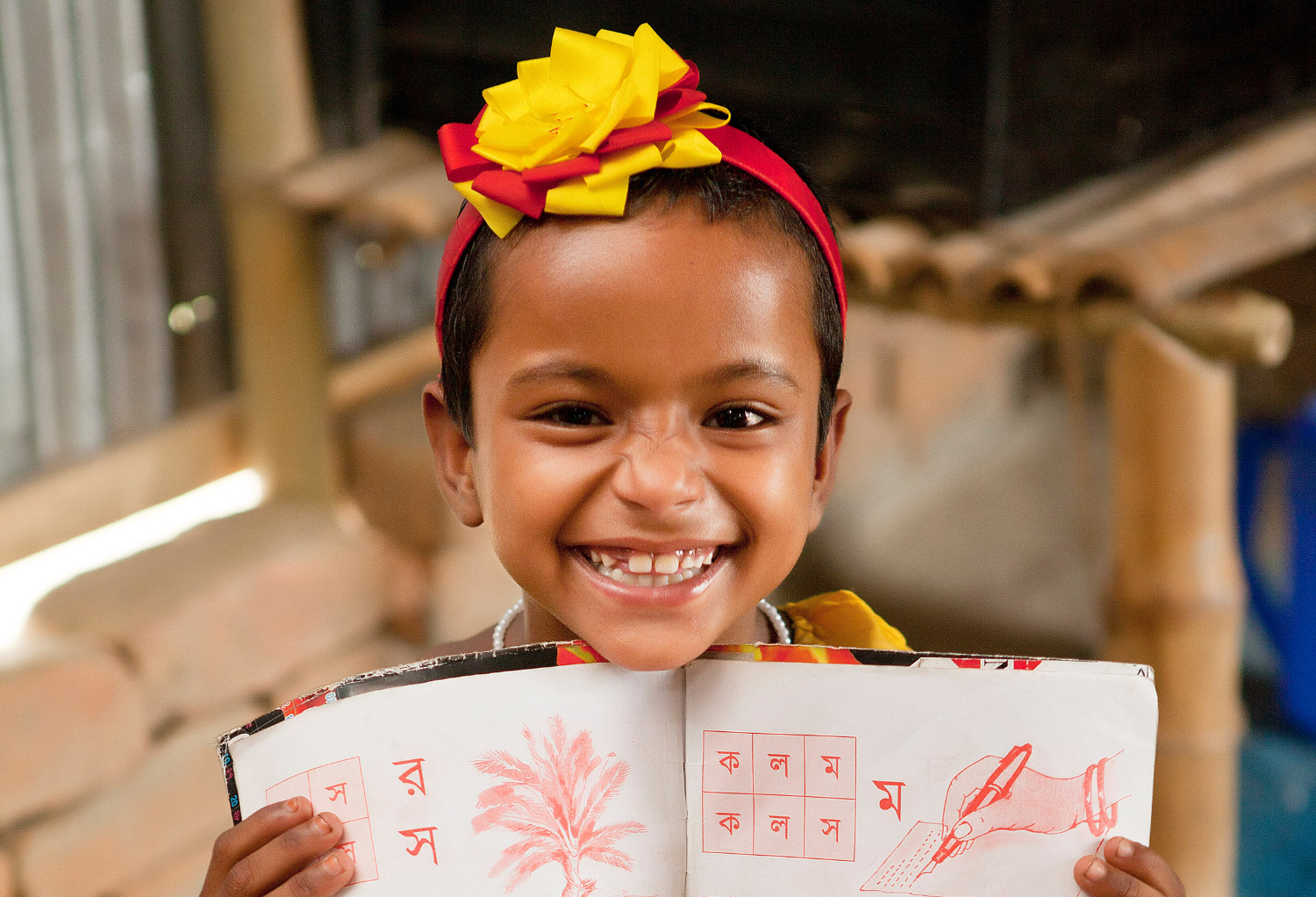 A girl holding up a workbook in a BRAC school with a big smile.