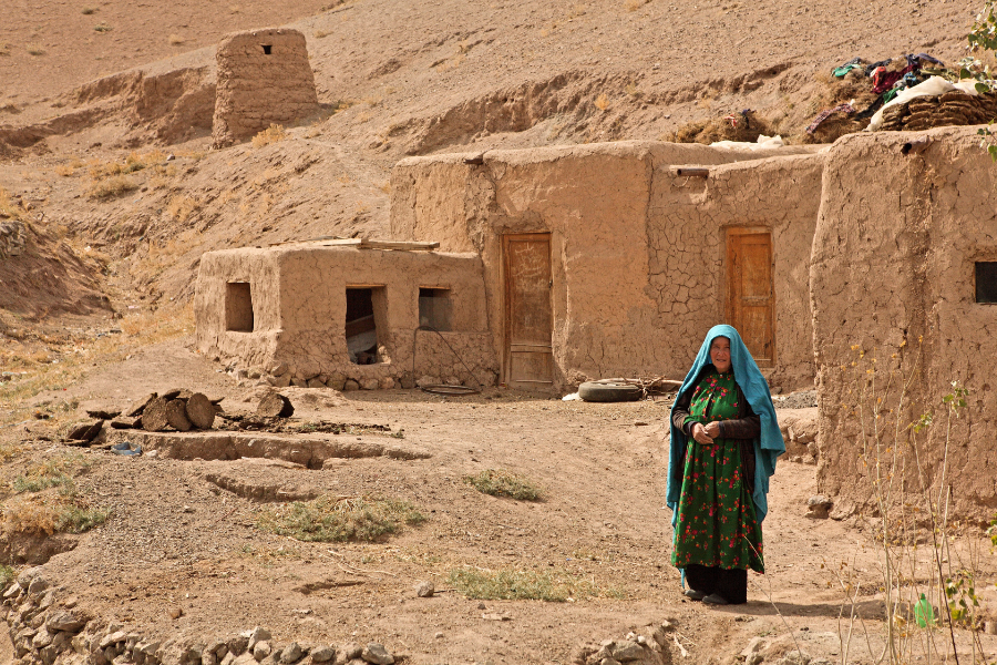 A woman stands in front of a home made of mud bricks in Afghanistan.