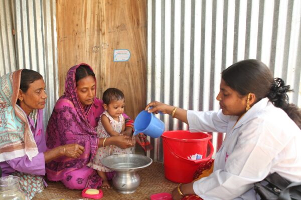A BRAC health worker visits the home of two women and a baby.