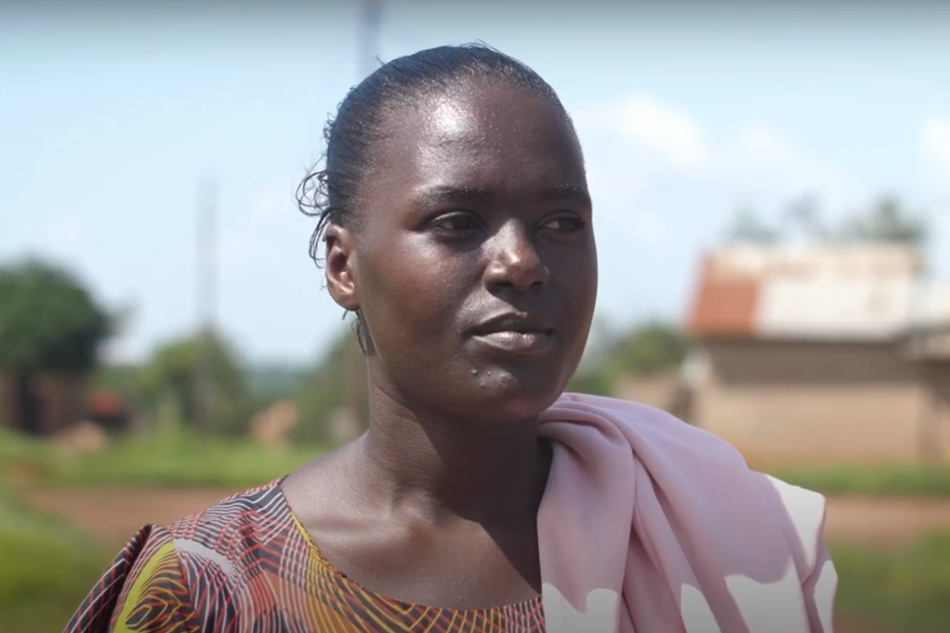 A close up portrait of Sarah, a young woman from Uganda, standing outside.
