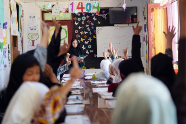 A classroom of female students in Afghanistan raising their hands