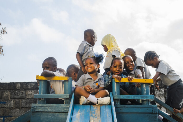 A group of children play on top of a play structure while one child sits atop the slide, about to slide down.