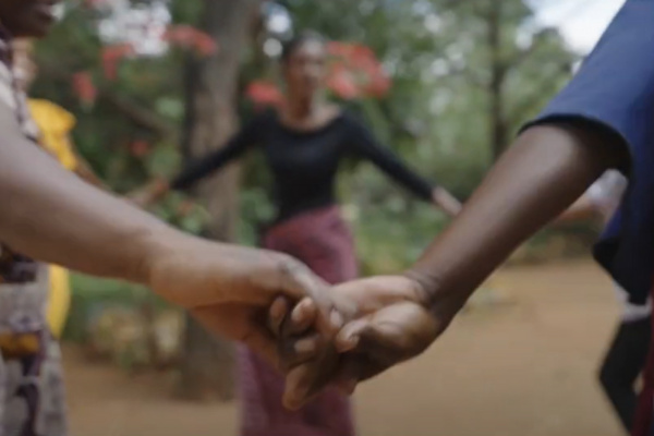 A blurry image of a group of girls in Africa holding hands together in a circle, zoomed in on two hands