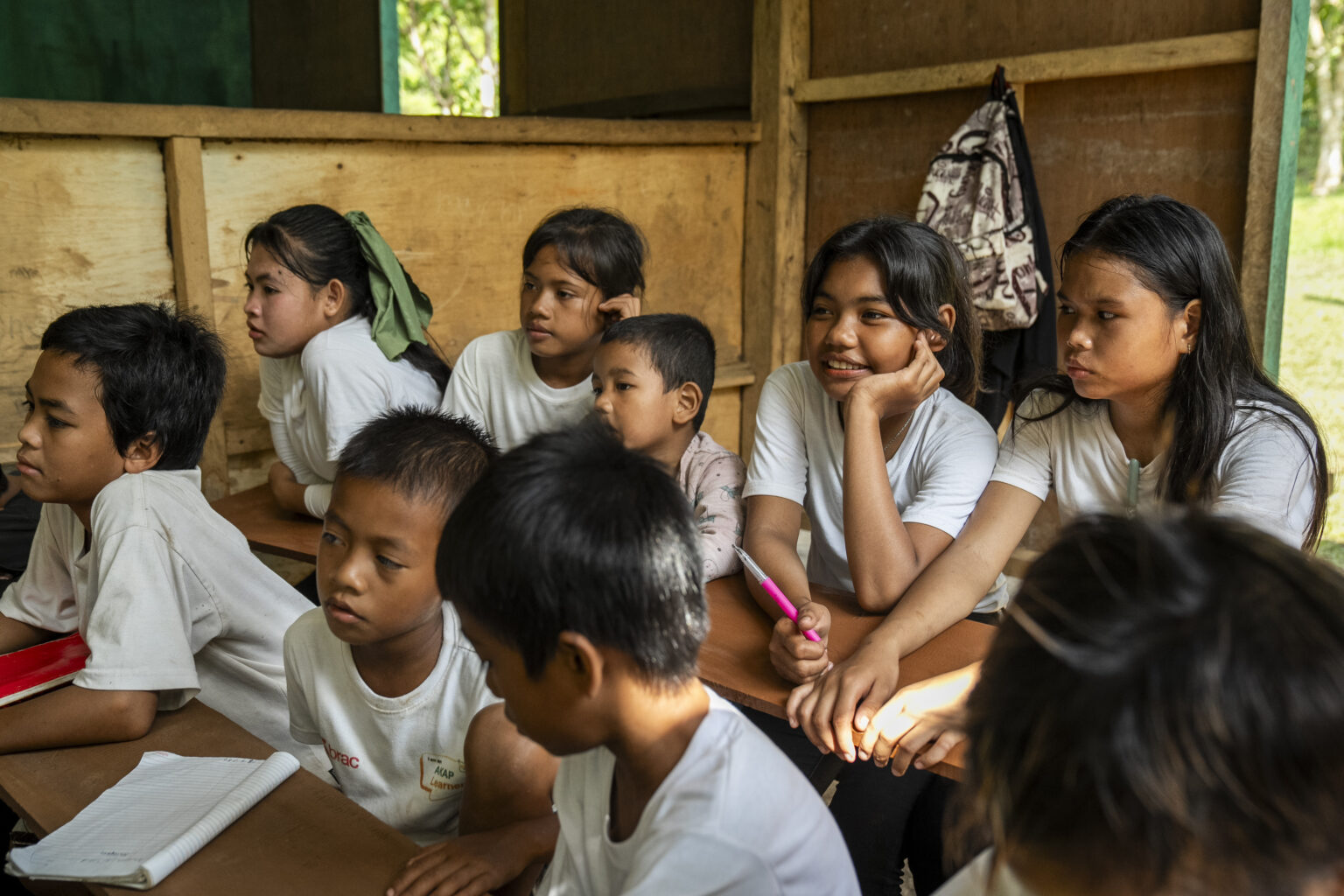 A group of children listen to the teacher while in a classroom, looking deep in concentration.
