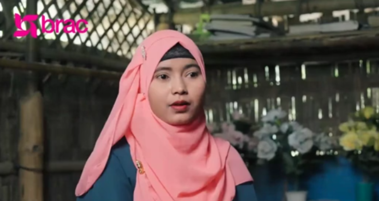 A woman who is a Rohingya refugee wearing a pink head scarf speaks to the camera.
